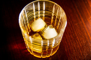 Honey whiskey on the rocks isolated on a dark wood background 