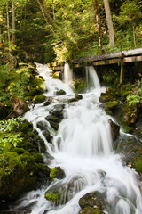 Naklejka na ściany i meble Wasserfall eines Baches mit Holzsteg und Langzeitbelichtung im Wald