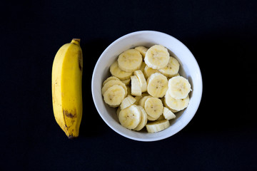 Banana prata picada em tigela  branca, com fundo preto.