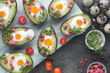 Keto diet dish: Avocado boats with ham cubes, quail eggs and cherry tomatoes on marble serving board