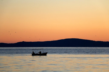 Silhouete of a small fishing boat and birds during suset. Beautiful sunset above the sea. 