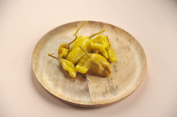 Canned hot jalapeno peppers on a wooden plate. Light background. Close-up.