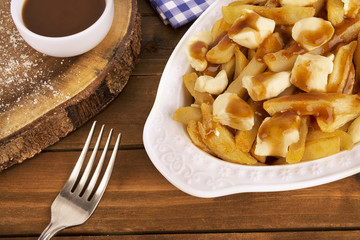 Poutine plate on a wooden background. Cooked with french fries, beef gravy and curd cheese....