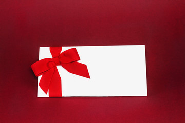 Isolated white gift card with red ribbon bow on deep red background.