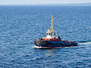 A tugboat navigates on the sea, in the background the coast can be seen 
