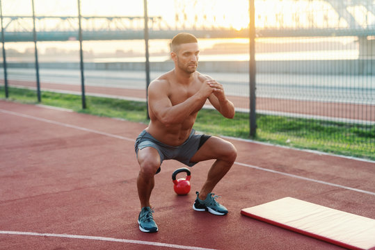 Shirtless Caucasian serious bodybuilder doing endurance in court in the morning. Next to him mat and kettlebell.