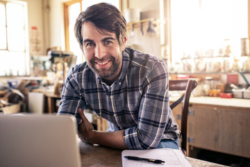 Woodworker smiling while using a laptop in his workshop