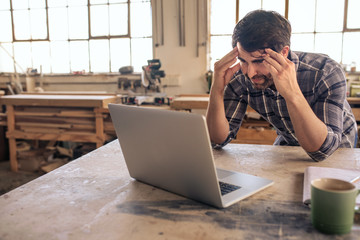 Stressed out woodworker using a laptop in his carpentry studio