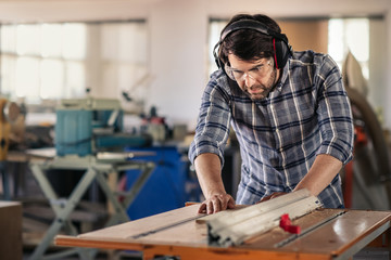 Carpenter sawing wood with a table saw in his workshop