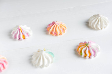 Pattern with meringues on a white wooden background. Multicolored meringues on a white background. Basis for confectionery banner, cafe, sweet shop. Meringue banner
