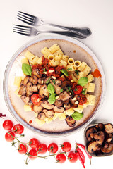Penne pasta rigatoni in tomato sauce with mushrooms, tomatoes decorated with parsley and basil