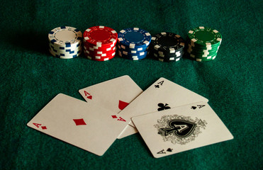 The four aces of a poker deck and poker chips of various colors on a green mat