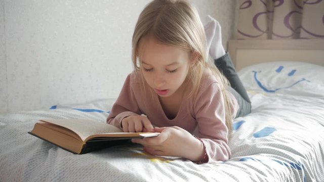 Girl child lay bed read book. Girl kid long hair cute pajamas relax and read fairytale book. Pleasant time in cozy bedroom.