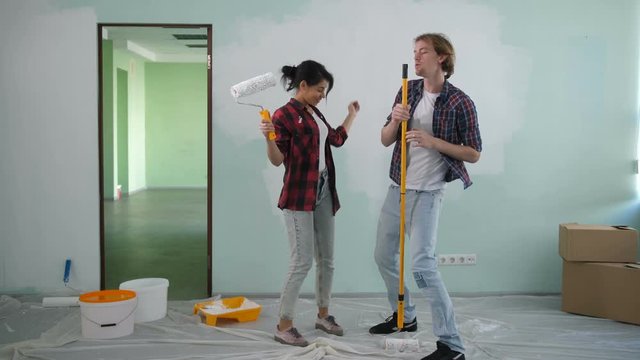 Renovation diy carefree couple in casual clothes relaxing, having fun and imagining themselves as rock star singing and dancing happily during home improvement and renewal design of new house.