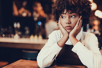 Upset waitress looking aside and touching her cheek by palm
