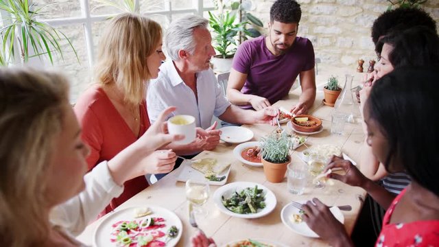 A multi-ethnic group of mixed age adult friends eating tapas together at lunch in a small restaurant, elevated view