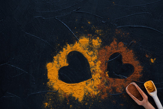 Two Hearts From Spices Curry Powder And Pepper Cayenne On Dark Background. St. Valentine's Day Concept.Overhead View.