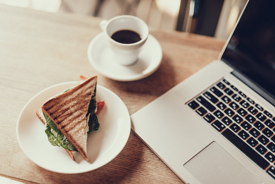 Netbook, sandvich and black coffee lying on table in cafe