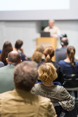 Male speaker giving presentation in lecture hall at university workshop. Audience in conference...