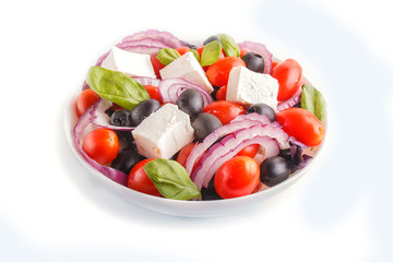 Greek salad with fresh cherry tomatoes, feta cheese, black olives, basil and onion isolated on...