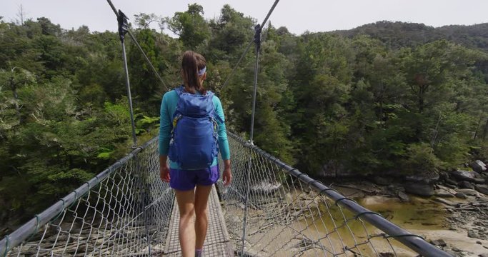 Hiking. Woman tramping in New Zealand, Abel Tasman National Park. Young traveller backpacking crossing swing bridge over Falls River. Shot on RED EPIC in SLOW MOTION.