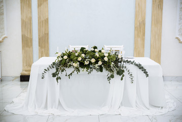 Wedding banquet. The festive table for the newlyweds is decorated with a beautiful composition of white roses and greenery