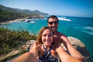 Fototapeta na wymiar happy couple taking selfie photo in front of the sea in Tayrona National Park, Tropical Colombia. Crazy tourists travelling on the white beach of caribbean sea. 