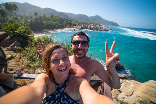 happy couple taking selfie photo in front of the sea in Tayrona National Park, Tropical Colombia. Crazy tourists travelling on the white beach of caribbean sea. 