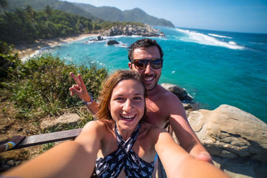 happy couple taking selfie photo in front of the sea in Tayrona National Park, Tropical Colombia. Crazy tourists travelling on the white beach of caribbean sea. 