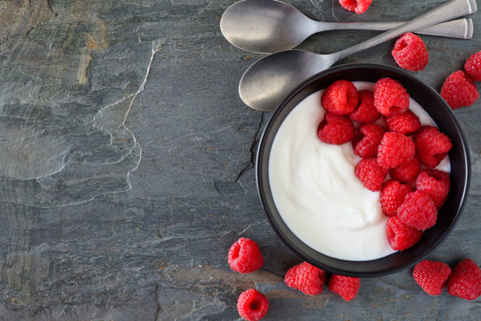 Bowl Of Yogurt With Raspberries. Top View, Side Border On A Dark Slate Background. Copy Space.