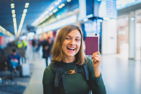 Beautiful young tourist girl in international airport, taking selfie with passport and boarding pass ready for boarding and fly. Doing gesture "ok" with other hand