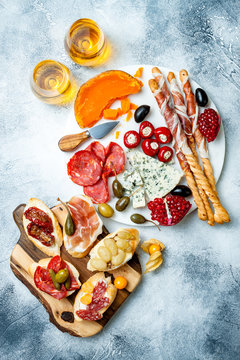 Appetizers table with antipasti snacks and wine in glasses. Brushetta or authentic traditional spanish tapas set, cheese and meat platter over grey concrete background. Top view