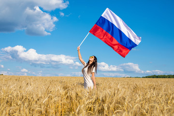 Young woman waving a Russian flag in a wheat golden field, summer outdoors