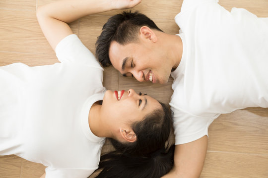 Asian couple looking at each other and lying on the floor at home, True love and Prewedding photography concept