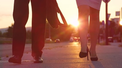 SLOW MOTION, LOW ANGLE, CLOSE UP, SUN FLARE: Unrecognizable man and woman in high heels walking to work at sunrise. Young business associates walking along the concrete sidewalk on a sunny evening.