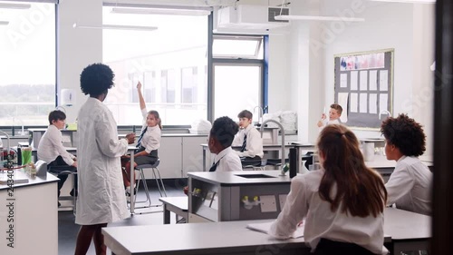 Female High School Tutor Teaching Students In Uniforms Sitting At