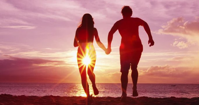 Beach couple holding hands on beach happy enjoying sunset running having fun on romantic summer travel vacation holiday honeymoon. Happiness and sunlight flare. RED EPIC SLOW MOTION.
