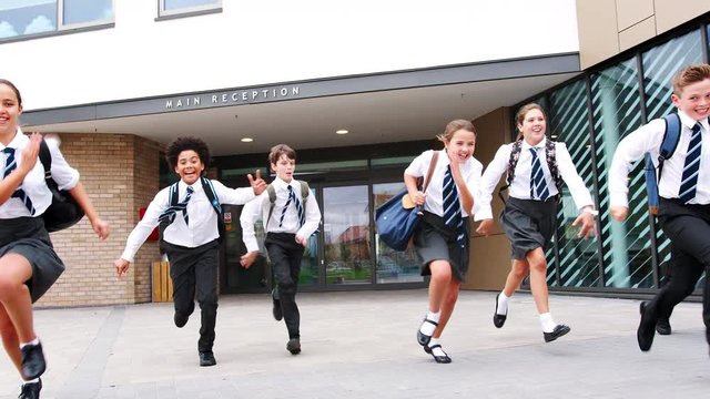 Group Of High School Students Wearing Uniform Running Out Of School Buildings Towards Camera At The End Of Class