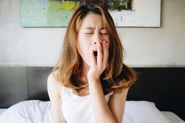 Portrait of sleepy woman yawing after her waking up in the early morning. Sitting in bed with messy...