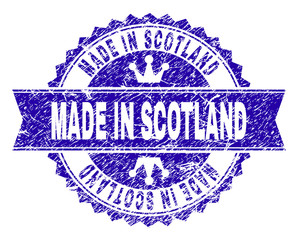 MADE IN SCOTLAND rosette stamp seal watermark with grunge texture. Designed with round rosette, ribbon and small crowns. Blue vector rubber print of MADE IN SCOTLAND title with grunge style.