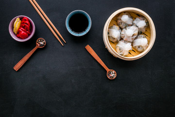 Chinese food set with dim sum, sticks and tea on black background top view copy space