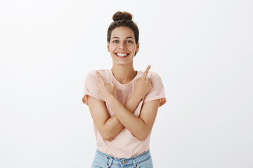 Obraz premium Optimistic good-looking friendly and young womanw ith tan and bright smile pointing sideways with arms crossed on body showing nice choices to try and buy grinning feeling confident and carefree