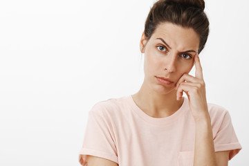 Close-up shot of concerned displeased young mother leaning on finger frowning and looking...