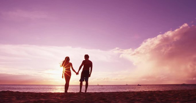 Couple at beach sunset romantic holding hands on beach on travel vacation.