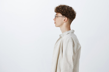 Profile shot of stylish handsome young hipster male freelancer with curly hairstyle in glasses...