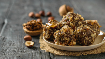 Walnuts and balls of nuts, dried fruits and chocolate on a black table.