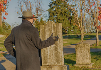 Aninymous man standing at a grave stone gesturing and mourning his loss