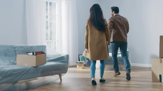 Excited Young Couple Holding Hands Enters Newly Purchased / Rented Apartment, They Start Happily Embracing and Dancing