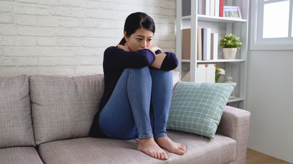 Pensive attractive woman sitting alone on sofa