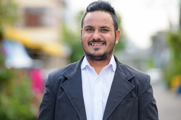 Naklejka premium Face of happy bearded Indian businessman smiling outdoors